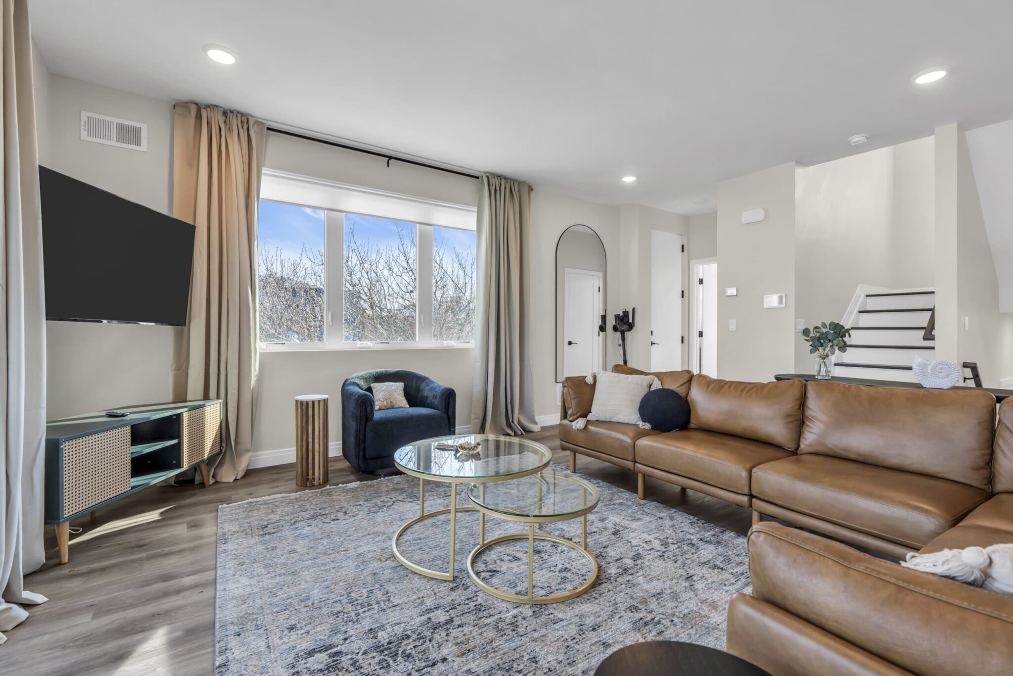 Modern living room with leather sectional sofa, glass coffee table, and large windows showcasing natural light, ideal for Jersey Shore vacation rentals.