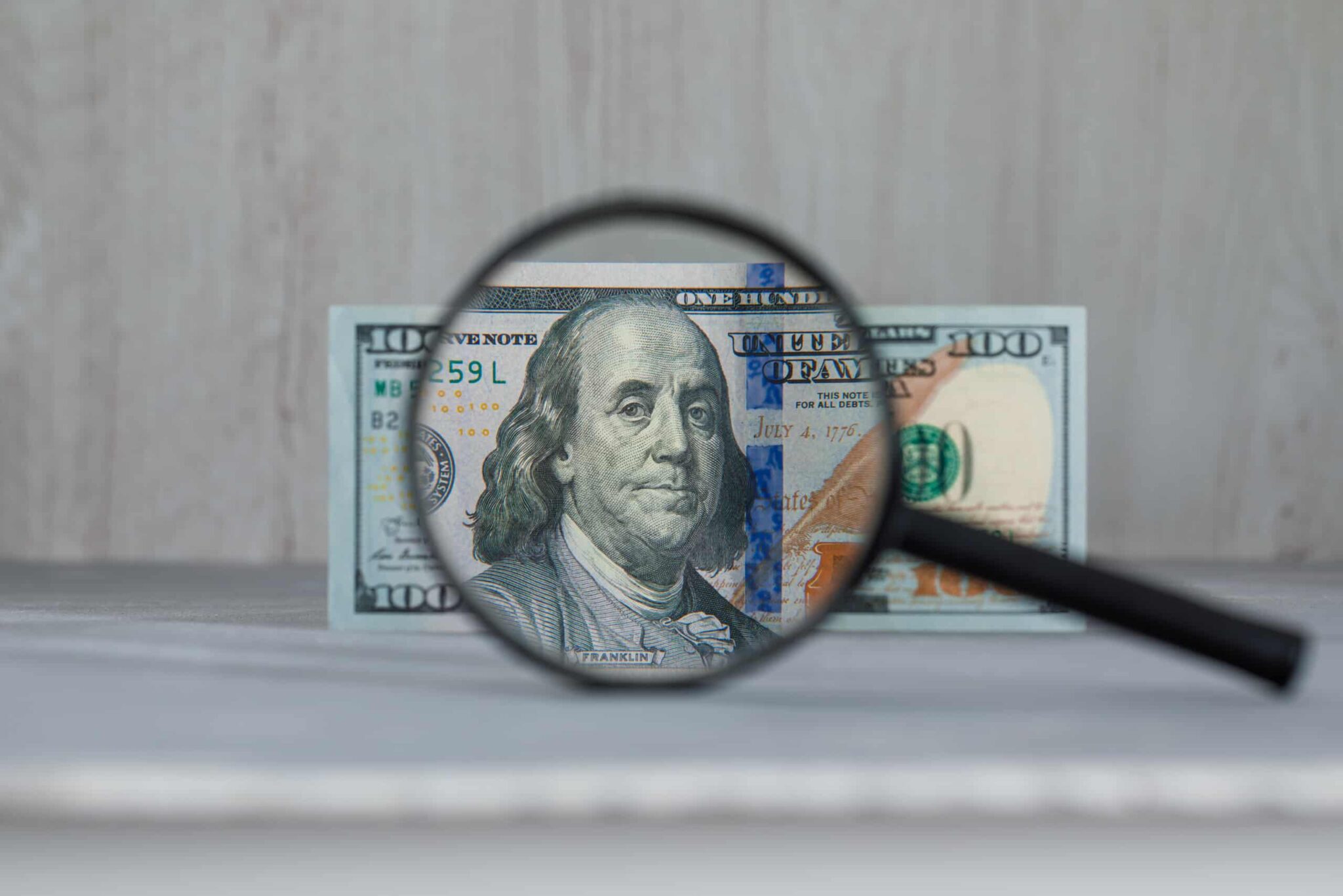 Magnifying glass focusing on a dollar banknote, symbolizing financial scrutiny and hidden costs in selling shore properties.
