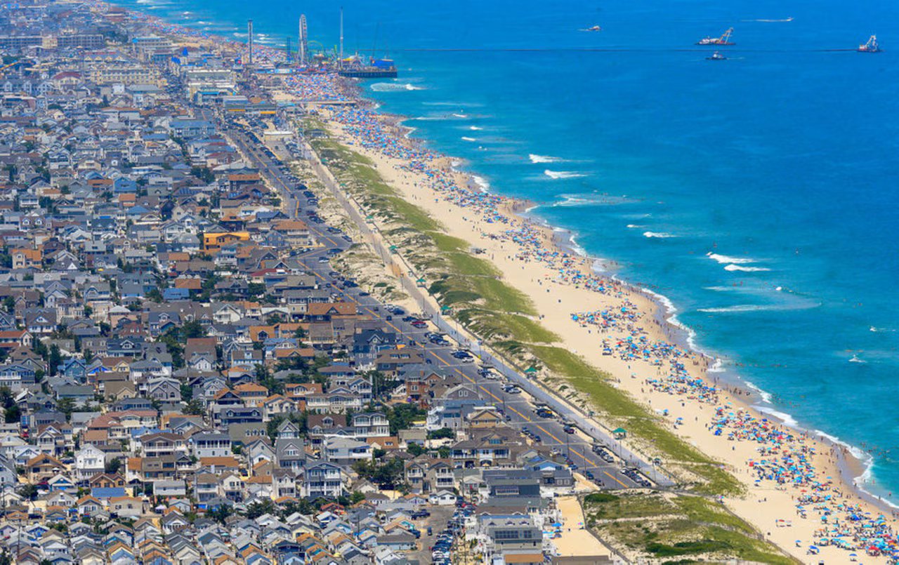 Aerial view of a bustling Jersey Shore beach with colorful umbrellas, sandy coastline, and nearby beach town, highlighting the vibrant summer atmosphere and popular vacation destination.