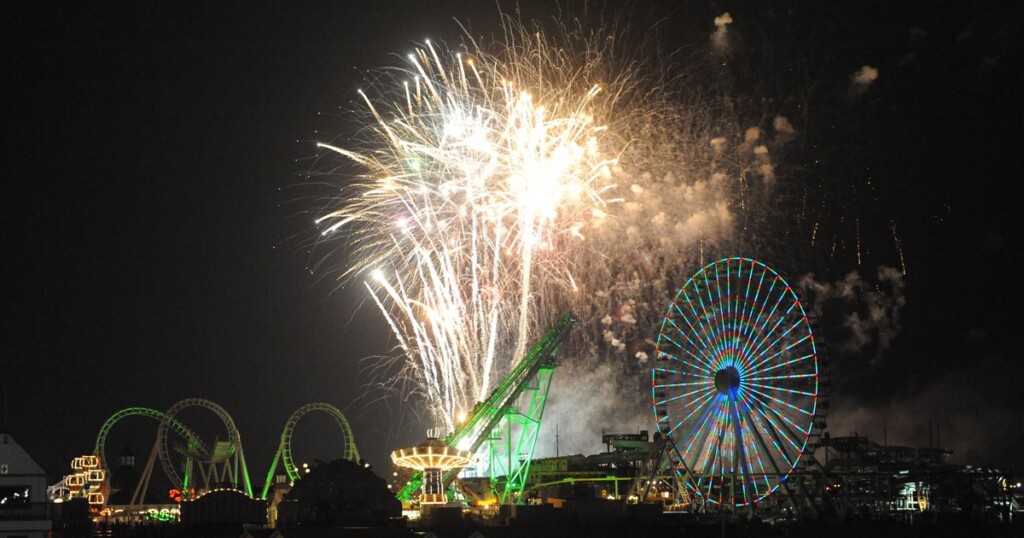 Fireworks display over Wildwood's amusement piers and boardwalk at night, featuring a colorful ferris wheel and vibrant rides, capturing the festive atmosphere of summer entertainment at the Jersey Shore.