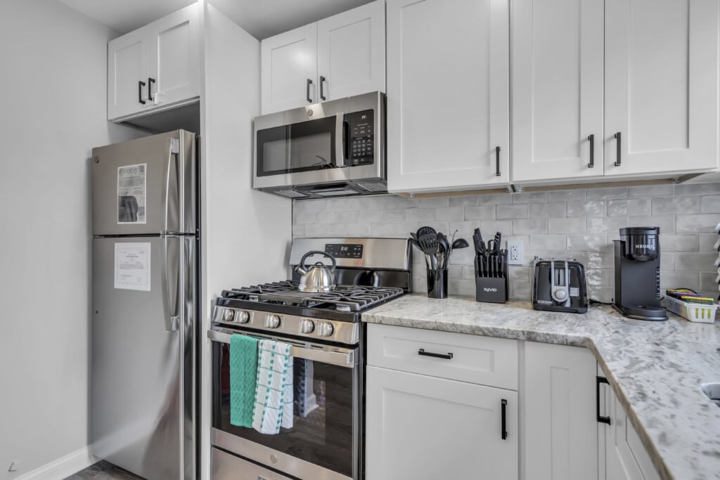 Modern kitchen with stainless steel appliances, including a refrigerator, microwave, and gas stove, showcasing coastal-themed decor and maintenance-friendly surfaces.