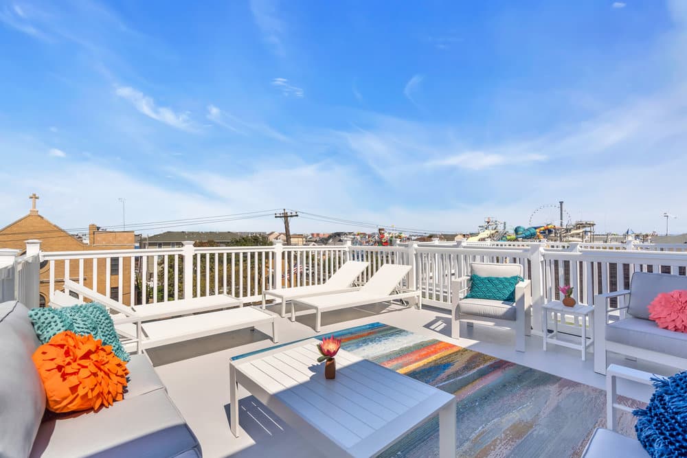 Modern beachfront vacation rental patio with colorful decor, seating area, and view of amusement rides at the Jersey Shore.