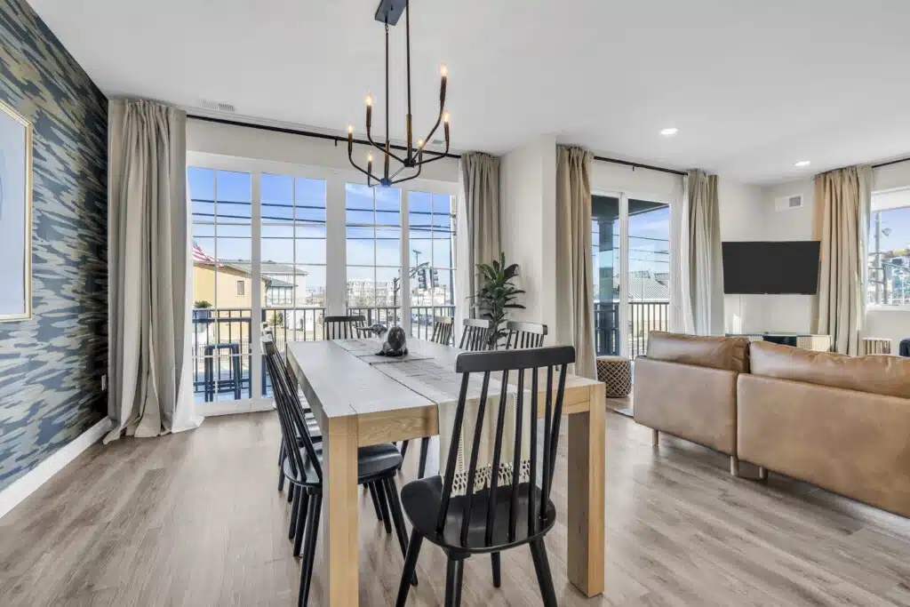 Modern dining area with a wooden table and black chairs, featuring large windows with beach views, stylish decor, and a cozy living space, ideal for showcasing Jersey Shore properties.