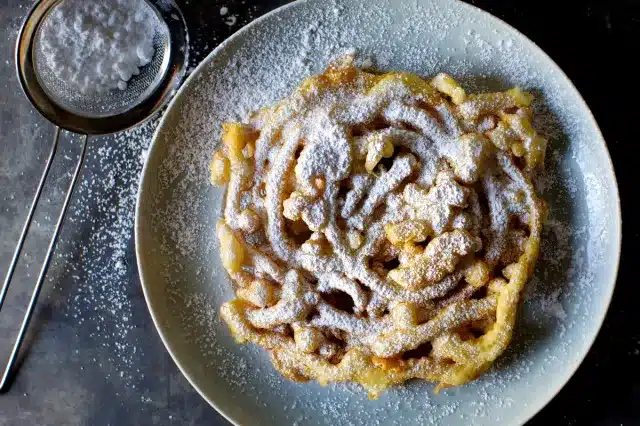 Funnel cake dusted with powdered sugar on a plate, symbolizing iconic Jersey Shore boardwalk food experience.