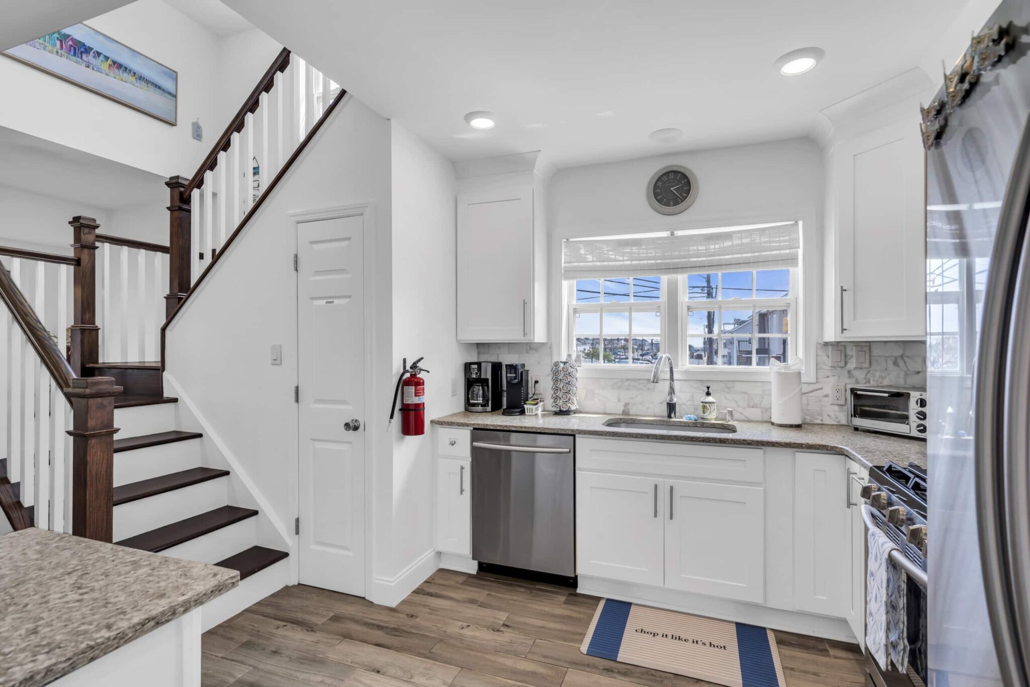 Modern kitchen interior in a Jersey Shore vacation rental, featuring white cabinetry, stainless steel appliances, and a view of the coastal environment through large windows, emphasizing maintenance and guest satisfaction.