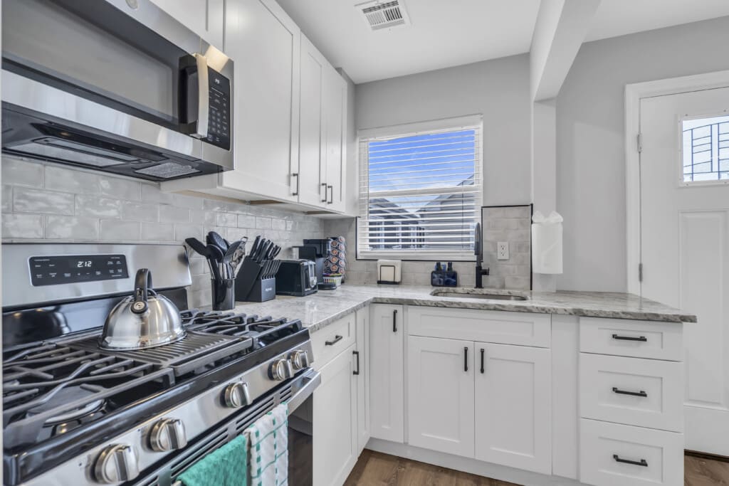 Modern kitchen with stainless steel appliances, including a gas stove and microwave, white cabinetry, granite countertops, and a window providing natural light, relevant for short-term rental property management in Seaside Heights.