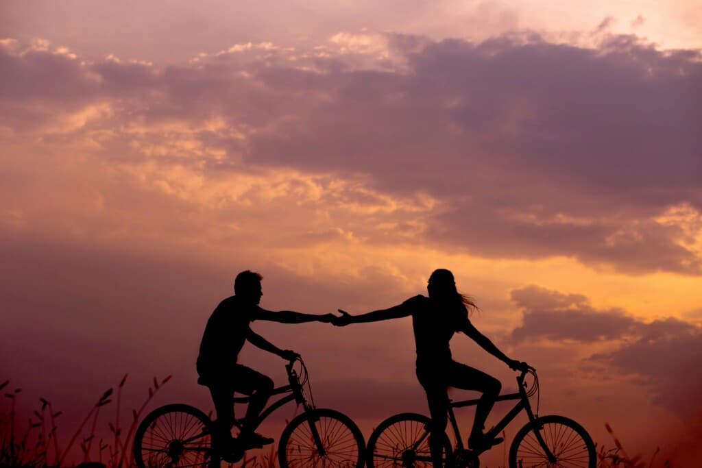 Couple riding bicycles at sunset, silhouetted against a colorful sky, symbolizing romance and adventure in Seaside Heights.