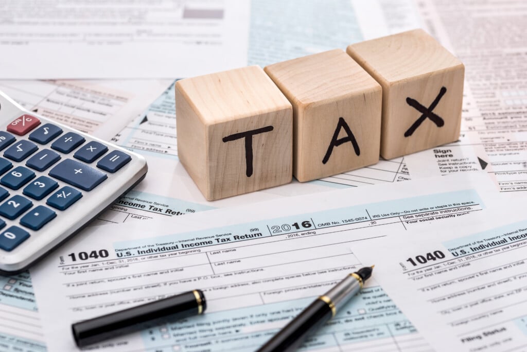 Wooden cubes spelling "TAX" next to a calculator and U.S. tax forms, illustrating tax considerations for vacation rental investments.