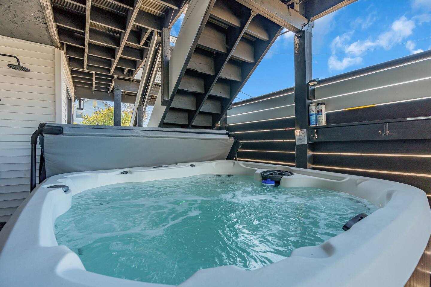 Hot tub with bubbling water under a wooden deck, surrounded by modern fencing, emphasizing luxury and relaxation for vacation rentals at the Jersey Shore.