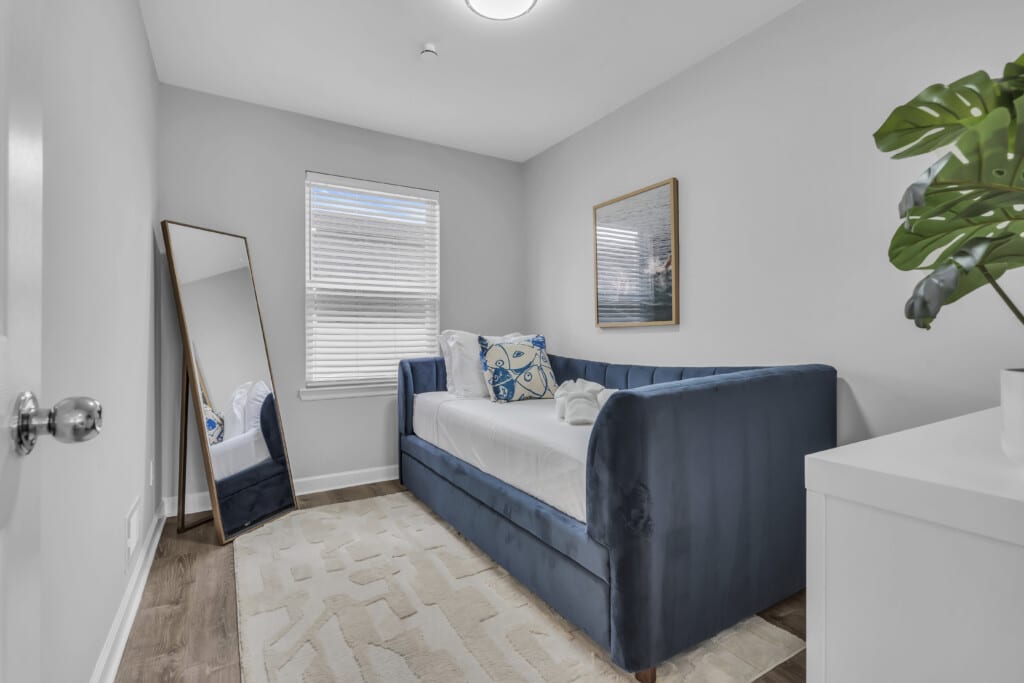 Cozy bedroom featuring a blue daybed with decorative pillows, a large mirror, and a bright window, ideal for Jersey Shore vacation rentals.