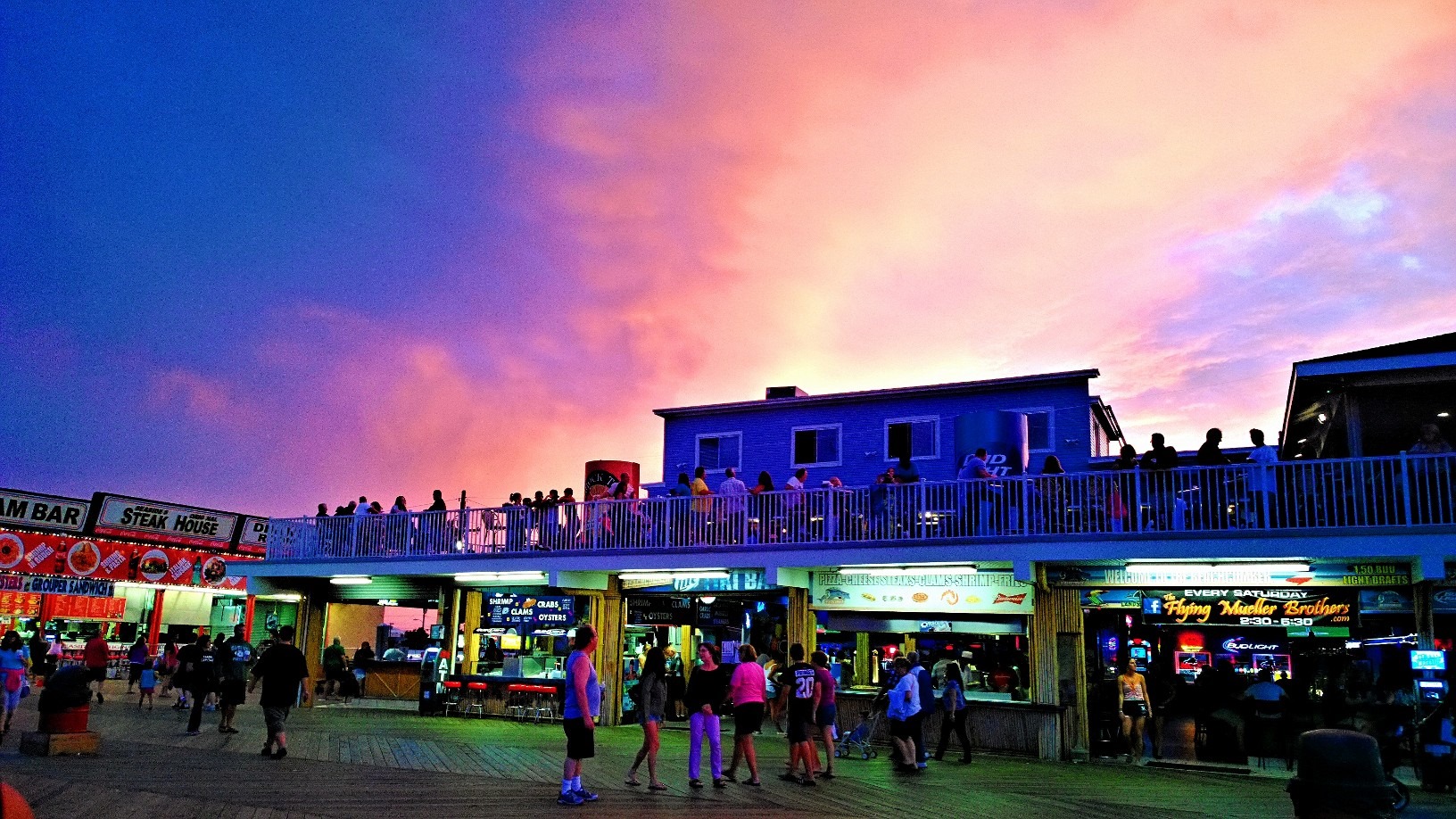 Seaside Heights boardwalk at dusk with vibrant sunset colors, bustling crowds enjoying bars and restaurants, capturing the lively nightlife atmosphere.