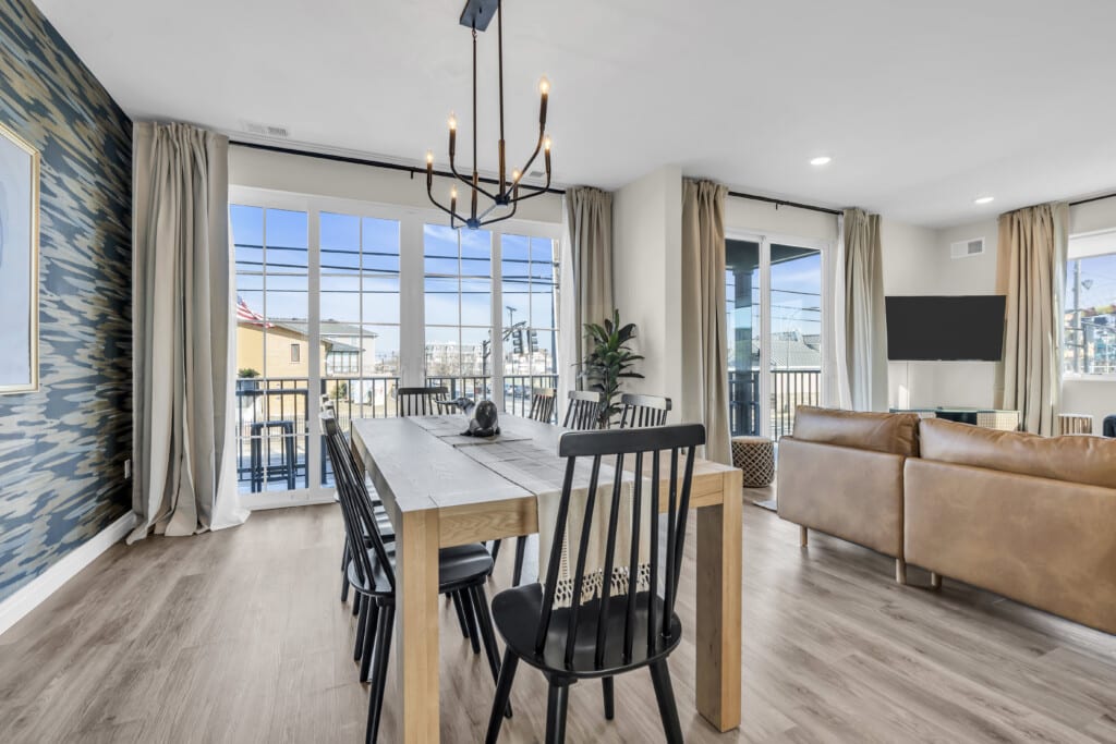 Modern dining area with a wooden table and black chairs, featuring large windows with beach views, stylish decor, and a cozy living space, ideal for showcasing Jersey Shore properties.