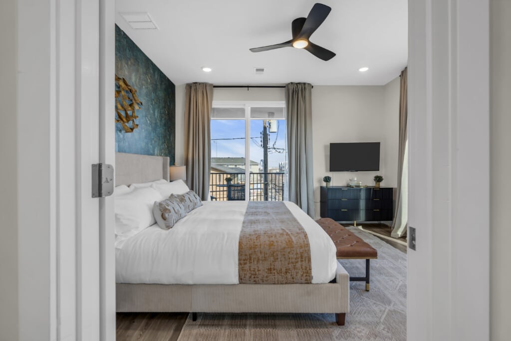 Modern bedroom with a king-sized bed, decorative pillows, stylish wall art, and a balcony view, emphasizing comfort and contemporary design for vacation rentals at the Jersey Shore.