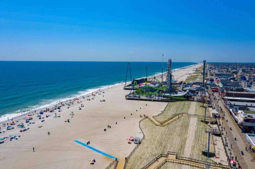 Aerial view of Seaside Heights beach with colorful umbrellas, Casino Pier amusement rides in the background, and visitors enjoying the vibrant Jersey Shore atmosphere.