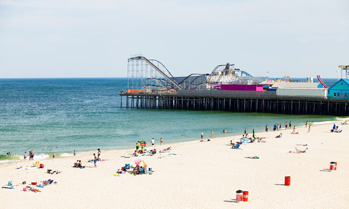 Seaside Heights beach with clean sand, people relaxing, and colorful boardwalk pier in the background, ideal for swimming and family activities.