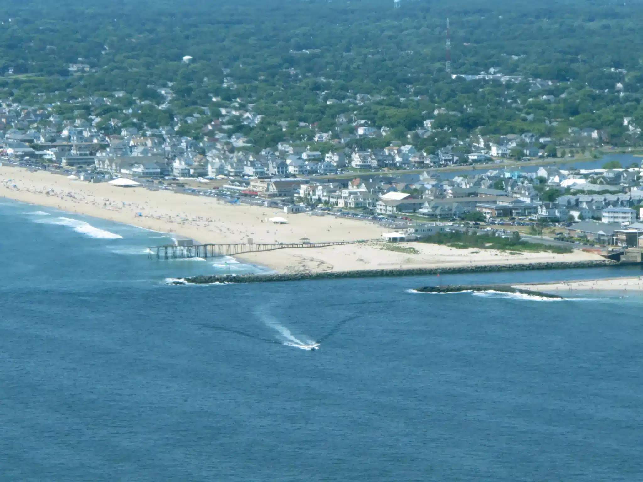 Aerial view of Belmar Beach, New Jersey, showcasing sandy shores, beachgoers, and the iconic boardwalk, emphasizing the town's appeal as a popular vacation destination.