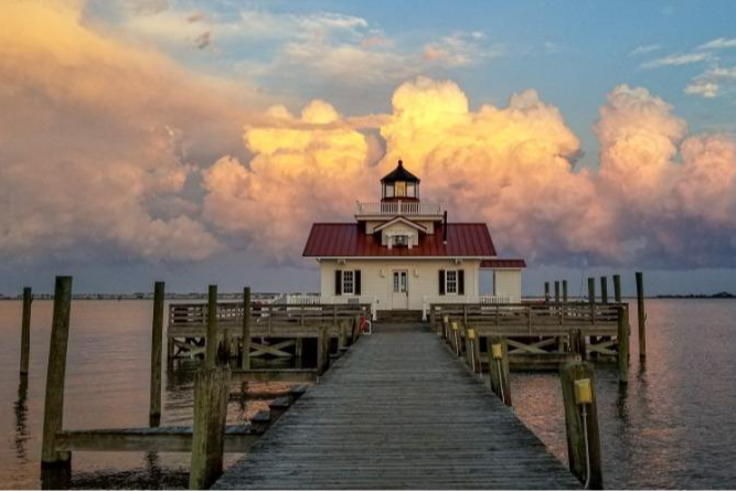 a smaller lighthouse on a pier with clouds in the sky