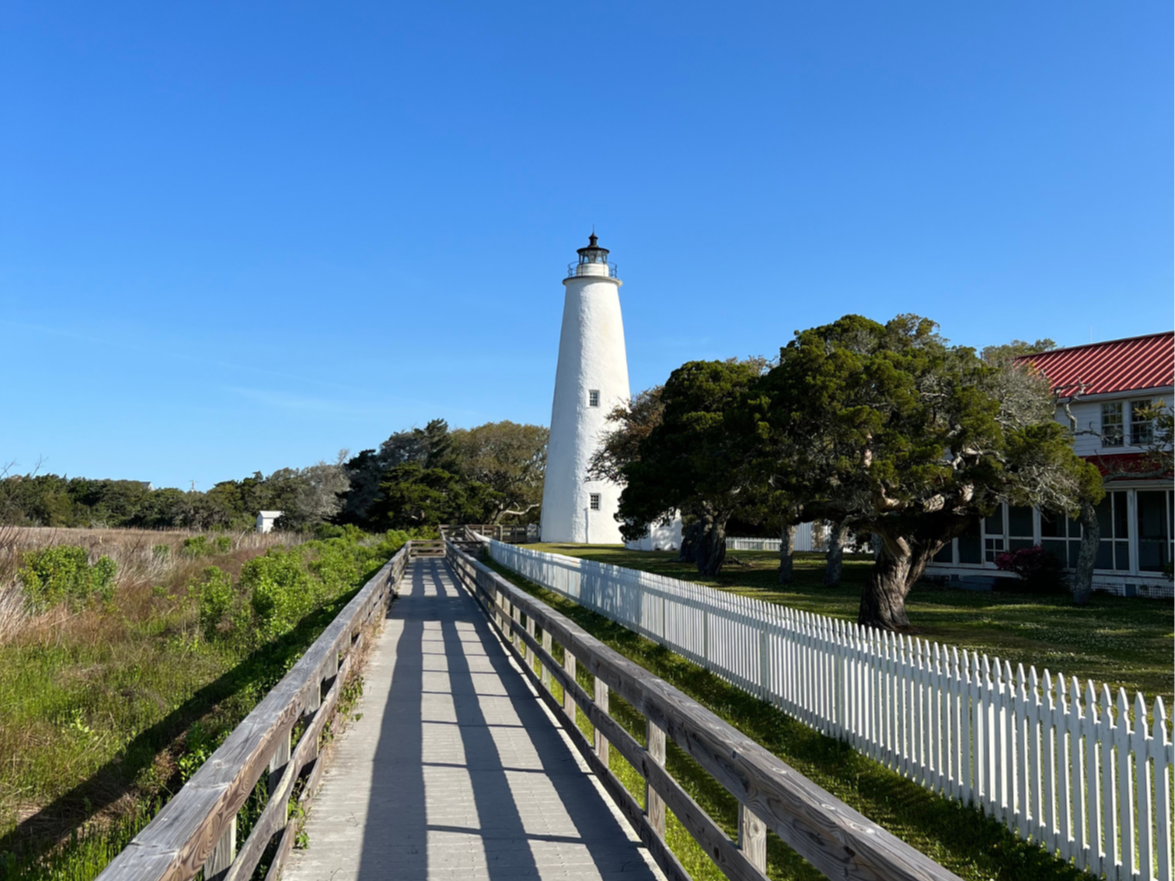 a boardwalk to a white lighthouse and house nextdoor