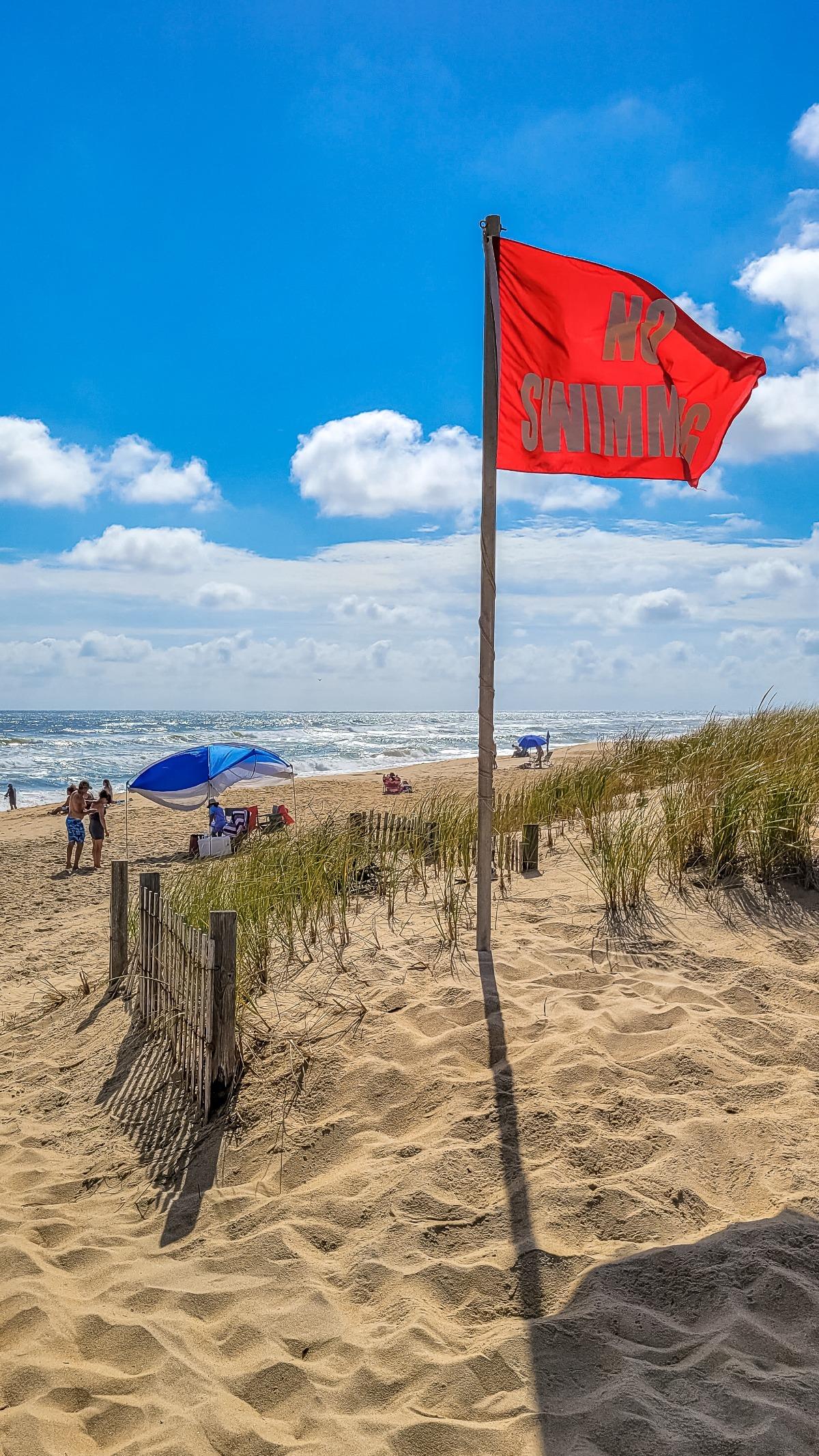 a red flag flying on the beach with rough surf