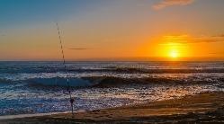 a fishing pole in the sand at the shoreline during sunrise