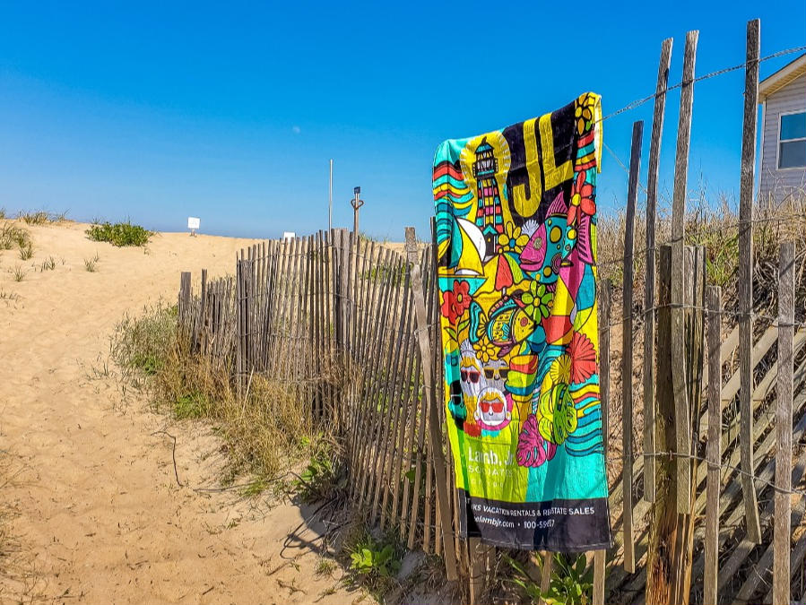 a beach towel hanging on a fence leading to the beach