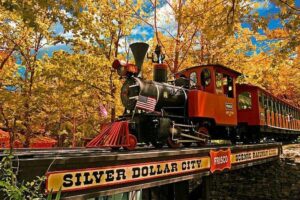 A train crosses a bridge, with a prominent sign reading "Silver Dollar City" visible in the scene.