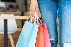 A woman stands in front of a table, holding several shopping bags, showcasing her recent purchases.