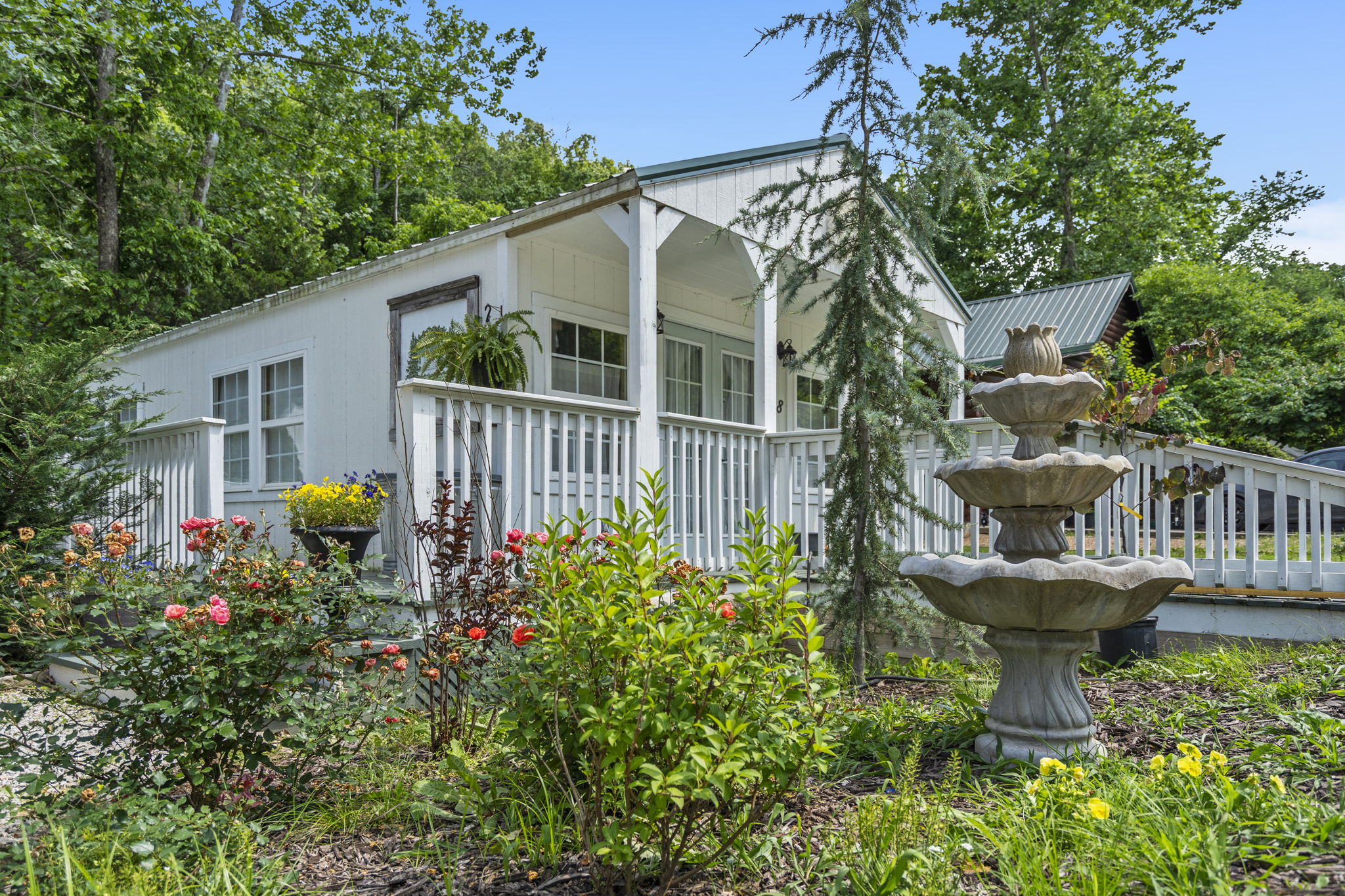 White cottage-style rental with a covered porch, rose garden and tiered stone fountain