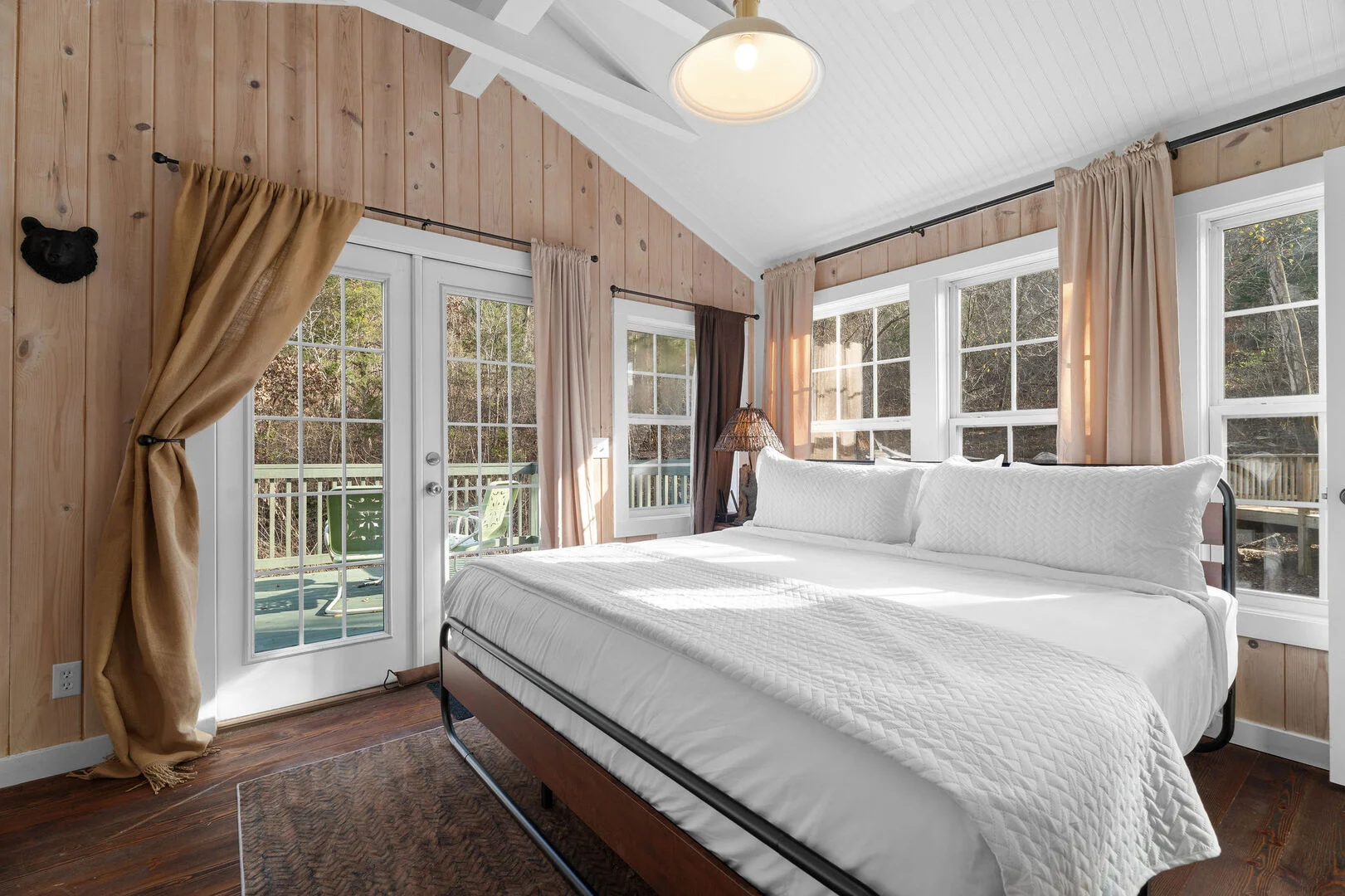 King bed beside glass doors to a wooded deck inside Serene Creekside Escape, a Branson cottage rental at Brushy Creek