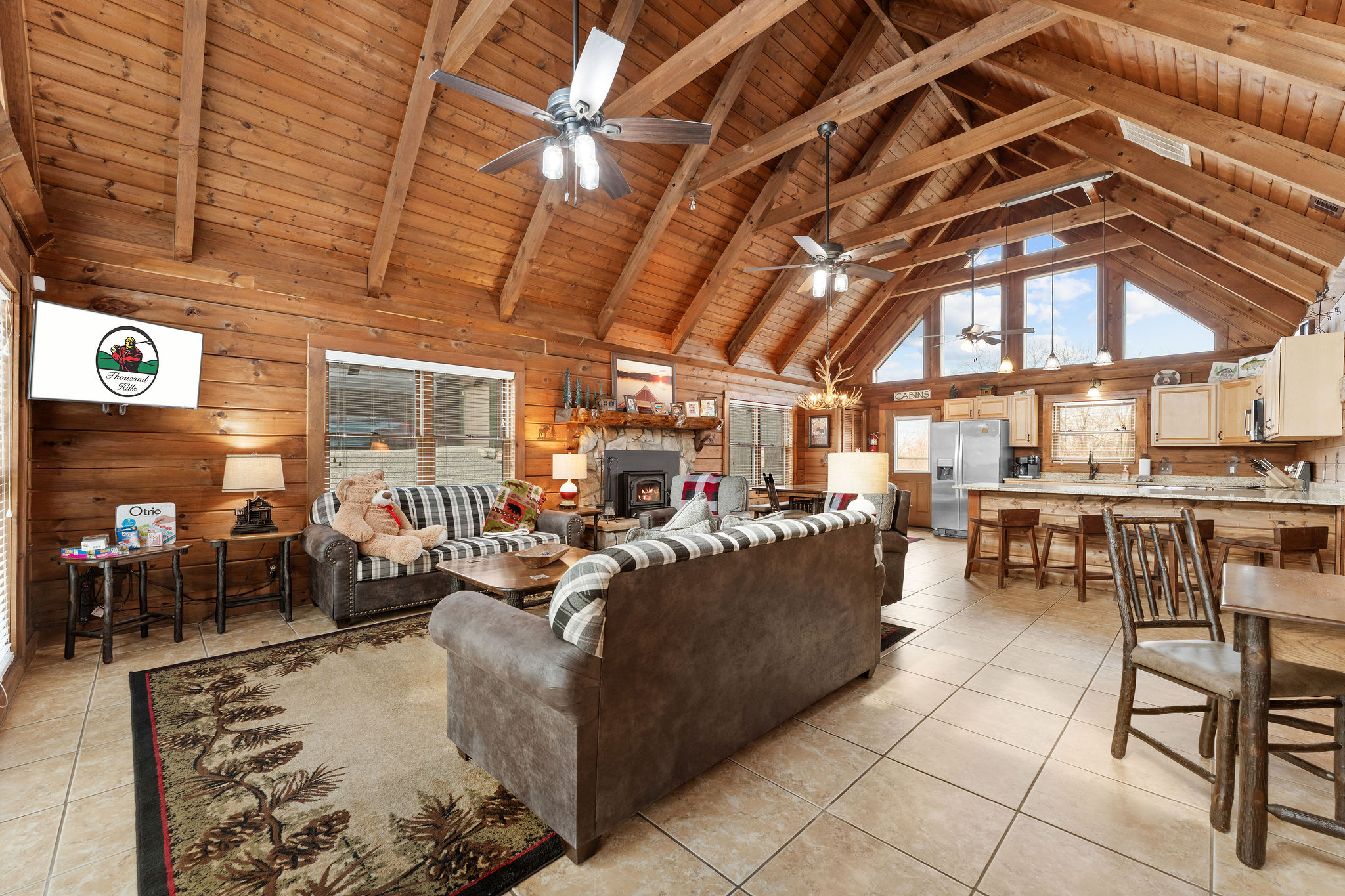 Log cabin great room with a vaulted wood ceiling, stone fireplace and open kitchen