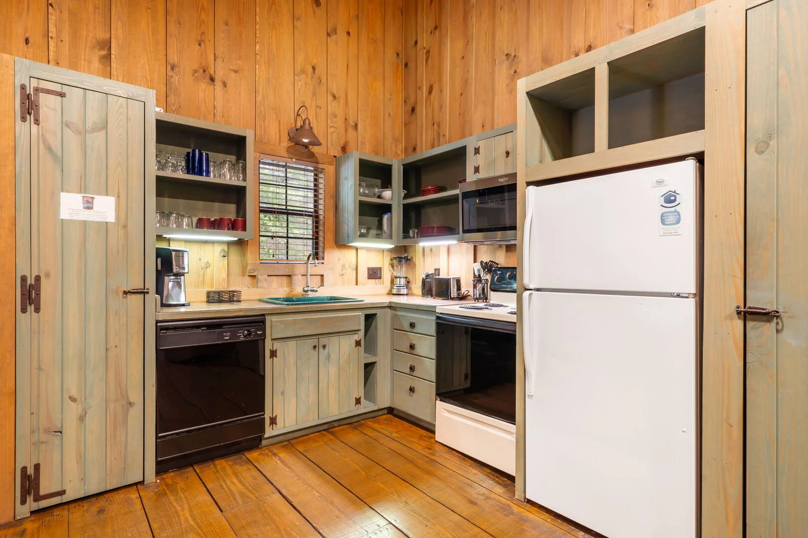 Full kitchen with an oven, refrigerator, dishwasher and open shelves of dishes inside a Cabins at Green Mountain log cabin in Branson, ready for cooking Thanksgiving dinner