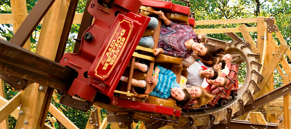 Riders on a red Silver Dollar City wooden roller coaster car banking through a timber track