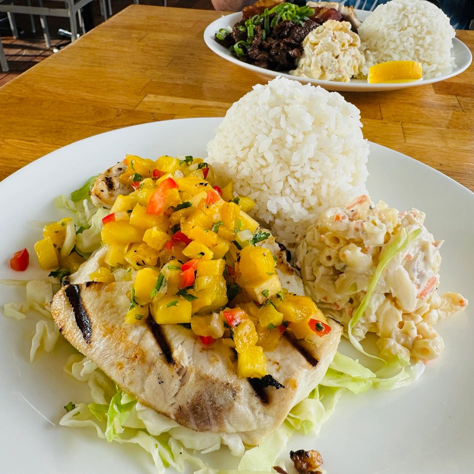 Grilled fish with pineapple salsa, rice, and macaroni salad on a white plate.